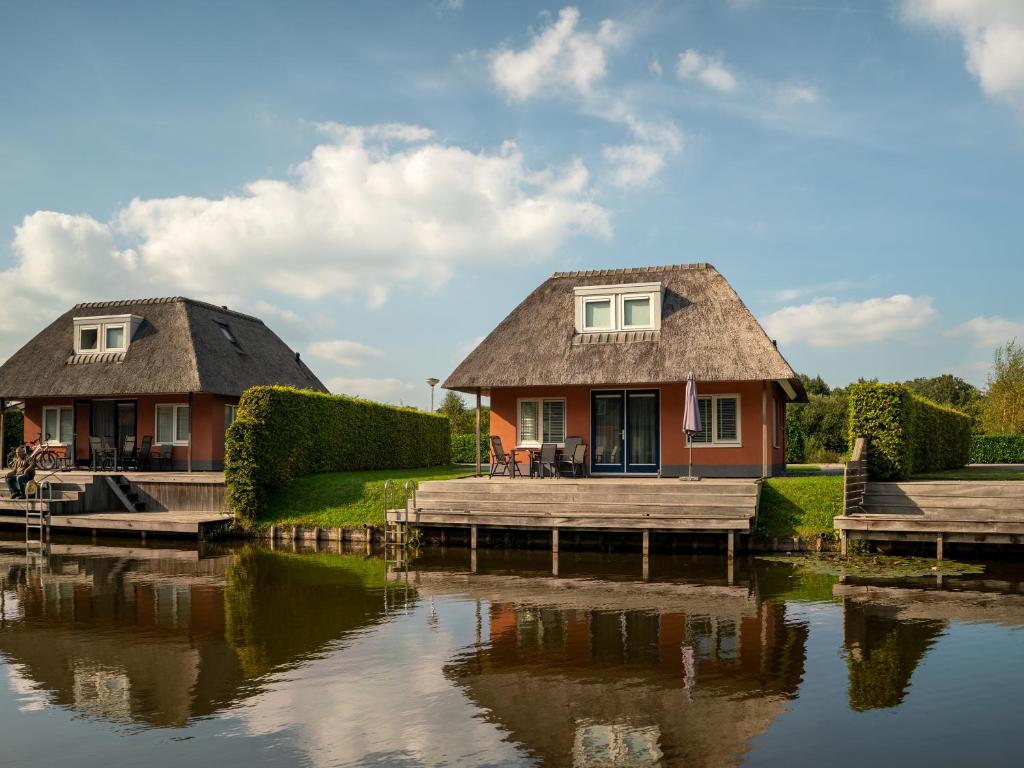 a house with a thatched roof next to a river at Summio Waterpark De Bloemert in Zuidlaren