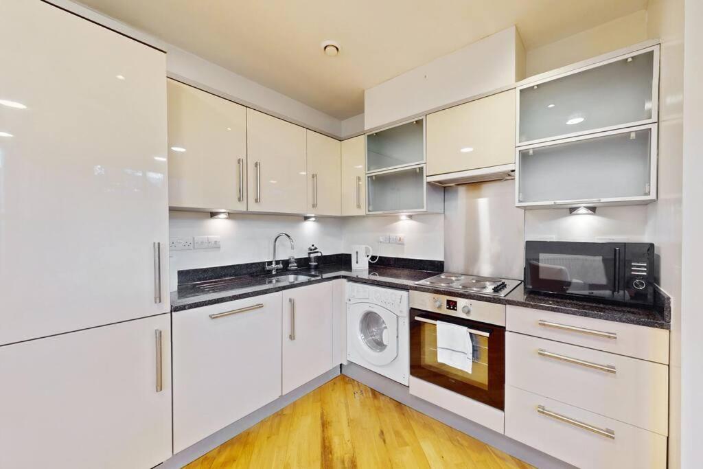 a kitchen with white cabinets and a microwave at Stunning 2 bed flat with a garden in New Cross in London