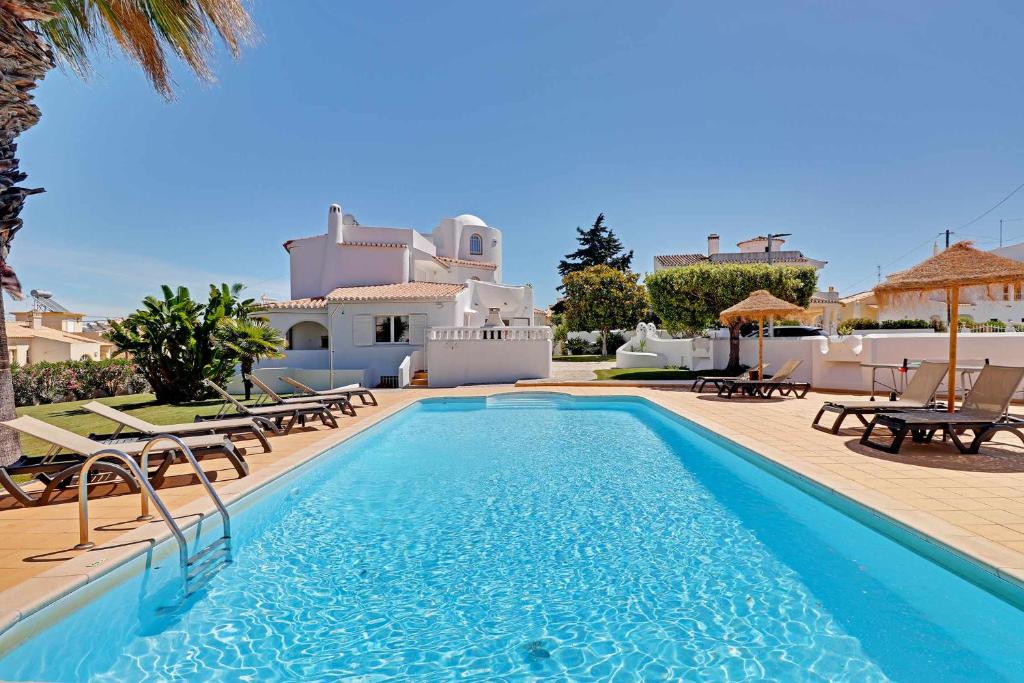 a pool with chairs and a villa in the background at Villux Vila Enar6 quartos ideal para familias in Albufeira