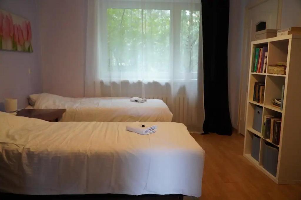 twee bedden in een kamer met een raam en een boekenplank bij Apartament Parterowy in Poznań