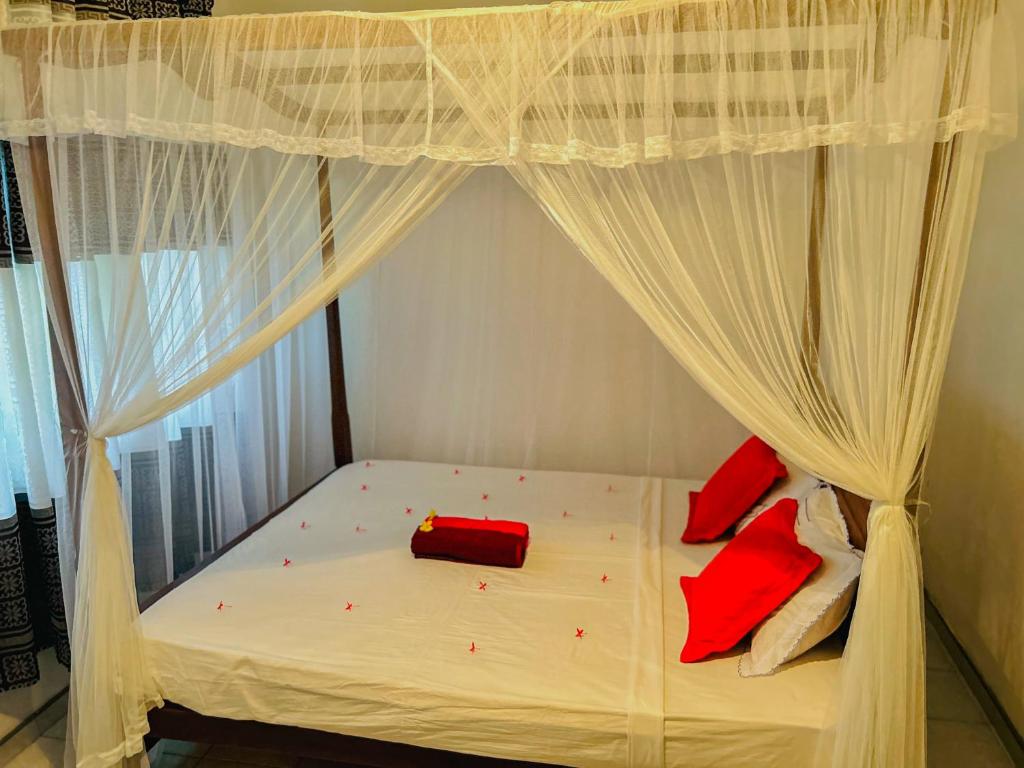 a bedroom with a canopy bed with red pillows on it at Kawshan Home Stay in Hiriketiya