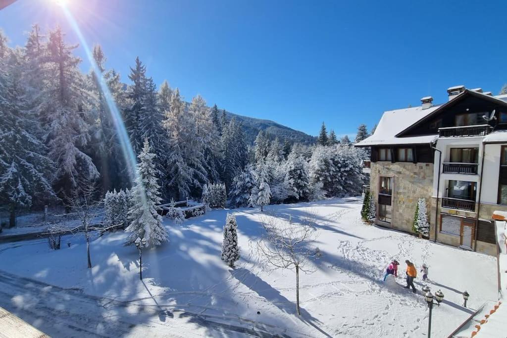 two people standing in the snow in front of a building at BH & Semiramida Ski Apartment in Borovets