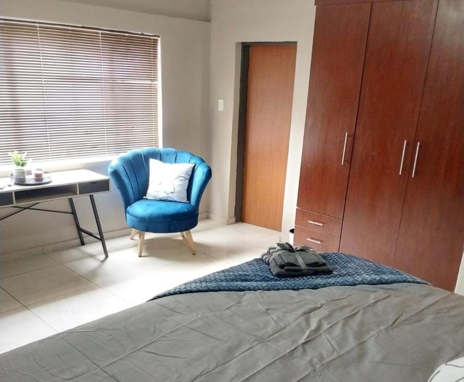 um quarto com uma cama, uma cadeira azul e uma secretária em Precious Estates Pearls em Zeerust