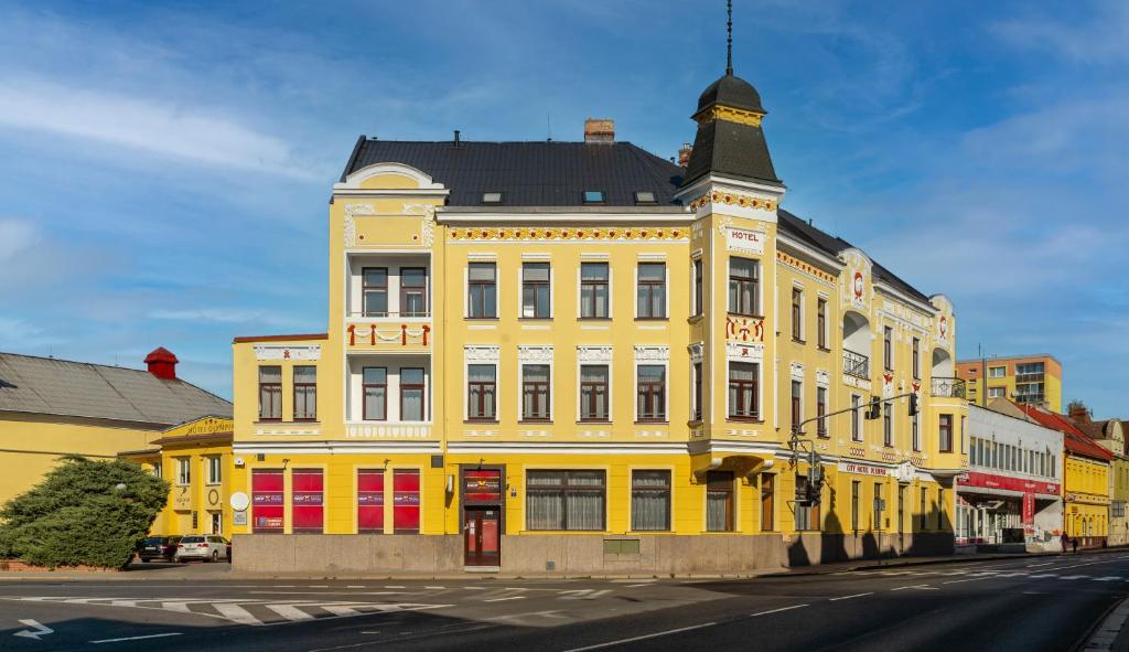 un bâtiment jaune avec un toit noir dans une rue dans l'établissement Hotel Olympia Česká Lípa, à Česká Lípa