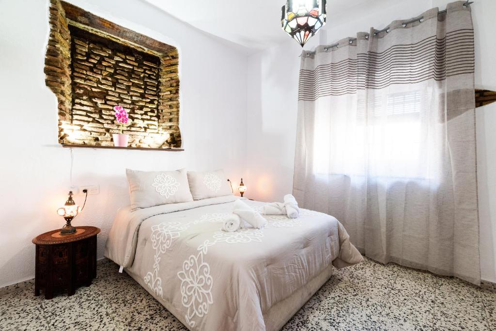 a white bedroom with a bed and a window at La casa del Sacristán. in Granada