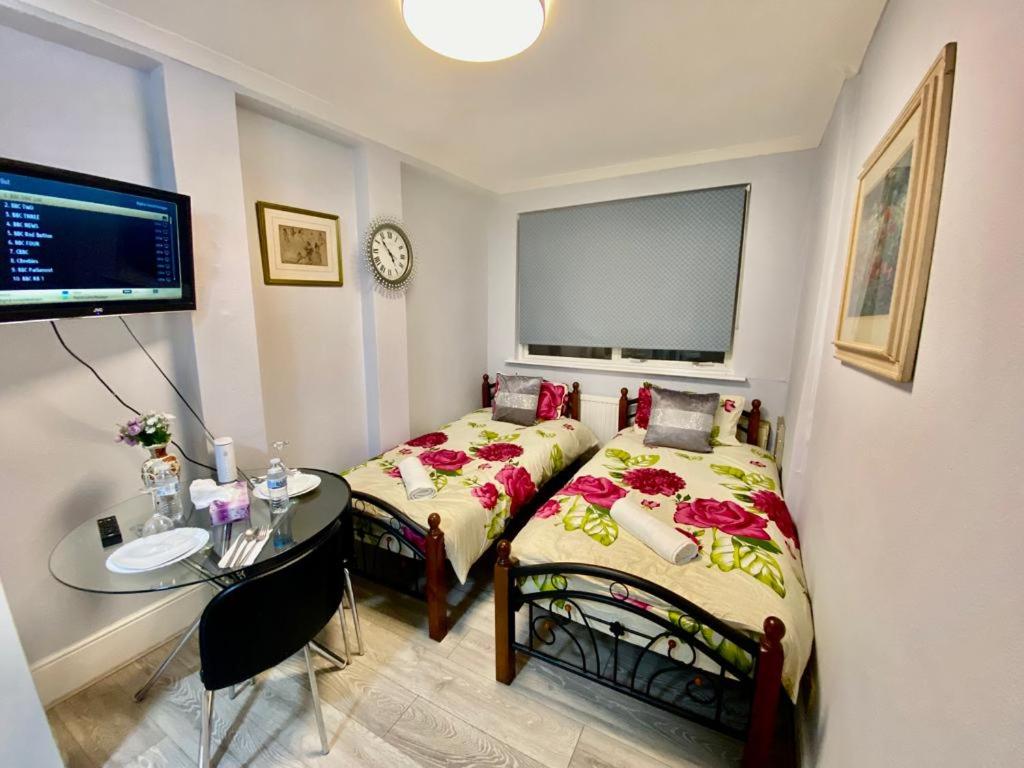 a bedroom with two beds and a table and a clock at Ground floor Studio Flat In London in London