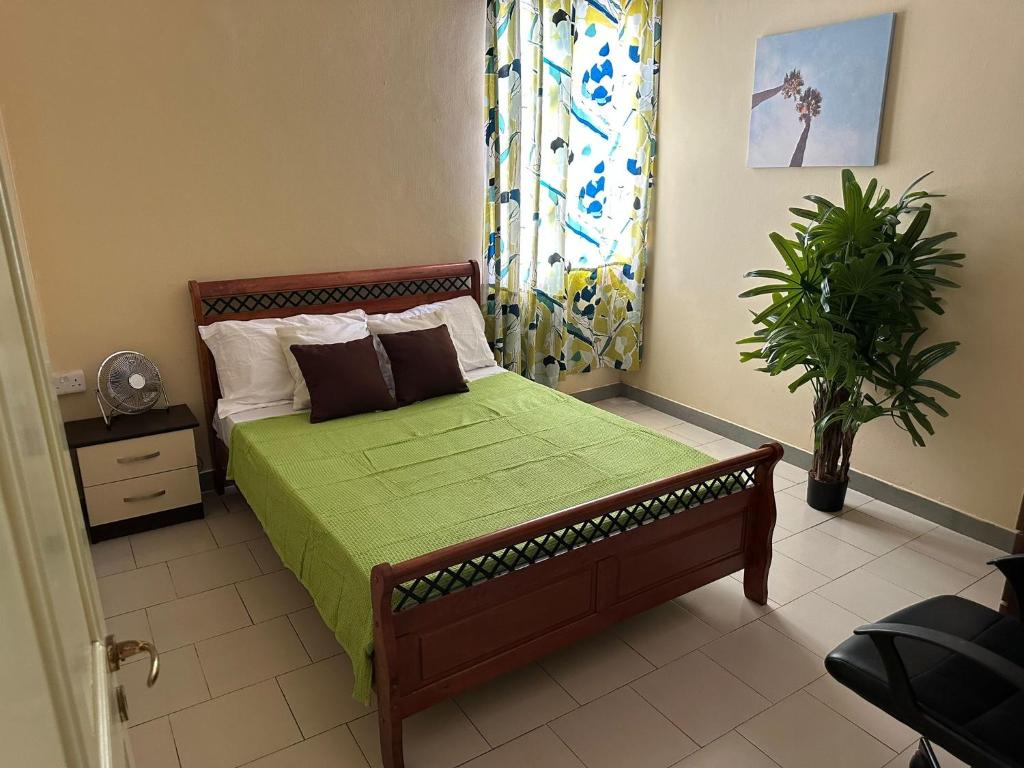 a bedroom with a bed with a green comforter and a plant at Baie du Tombeau Apartment in Baie du Tombeau