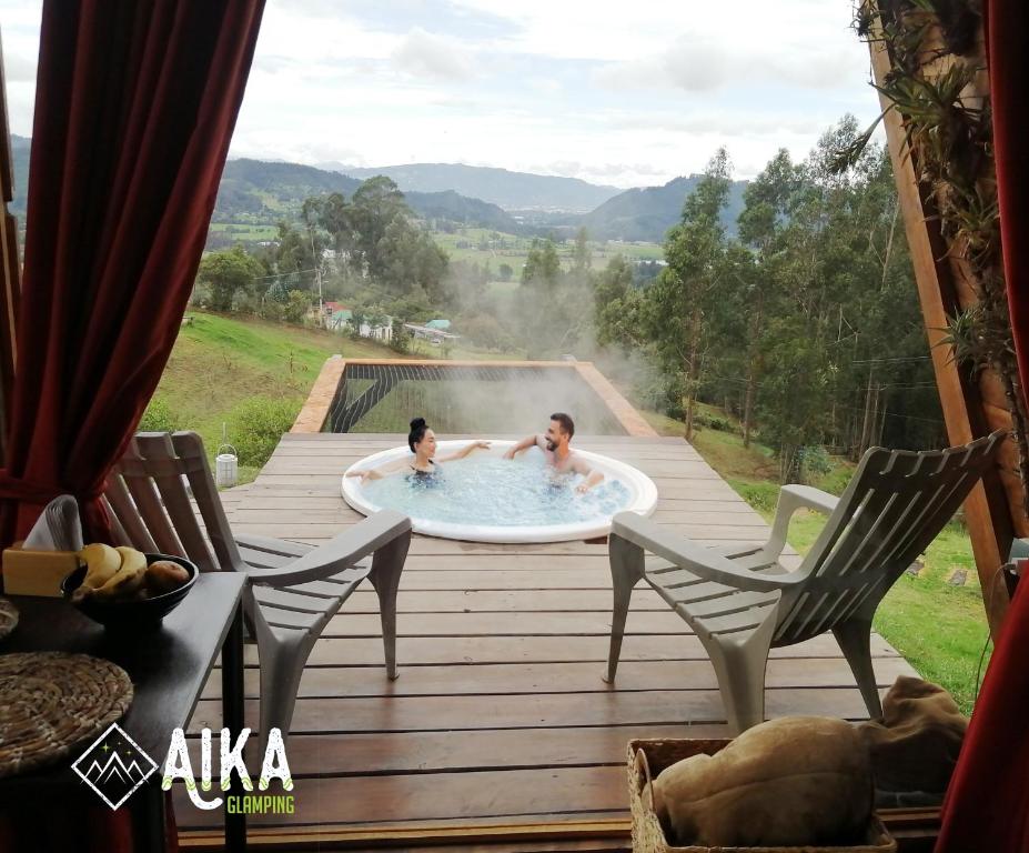 2 personas en una bañera de hidromasaje en una terraza de madera en AIKA Reserva Glamping Tabio, en Tabio