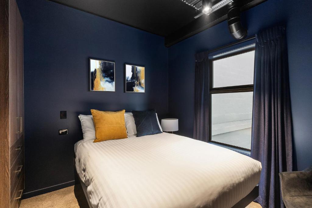 a blue bedroom with a bed and a window at Abstract Hotel & Residences in Auckland