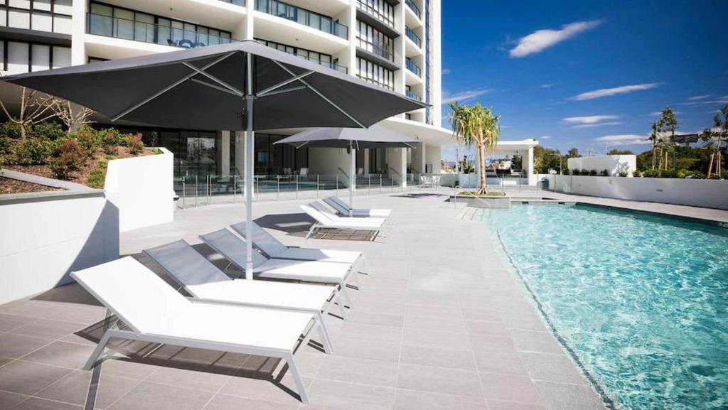 uma piscina com espreguiçadeiras e um guarda-sol ao lado de um edifício em Large Ocean Views 4BR Sub-Penthouse - Sierra Grand em Gold Coast
