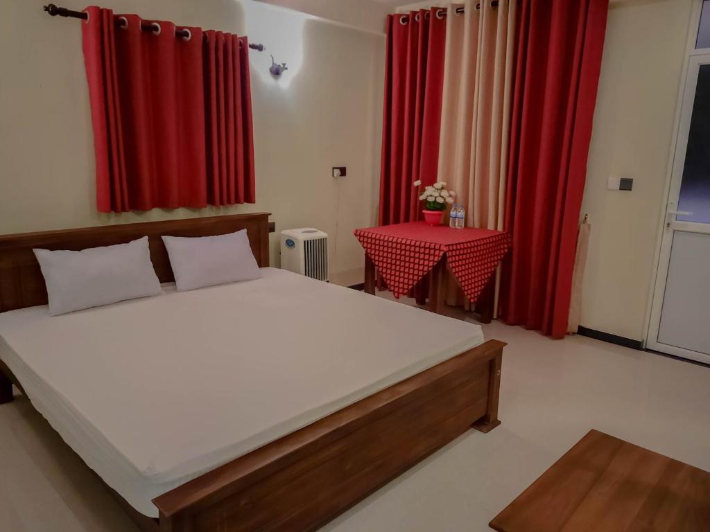 1 dormitorio con cama, mesa y cortinas rojas en Eventide Beach Resort en Marawila