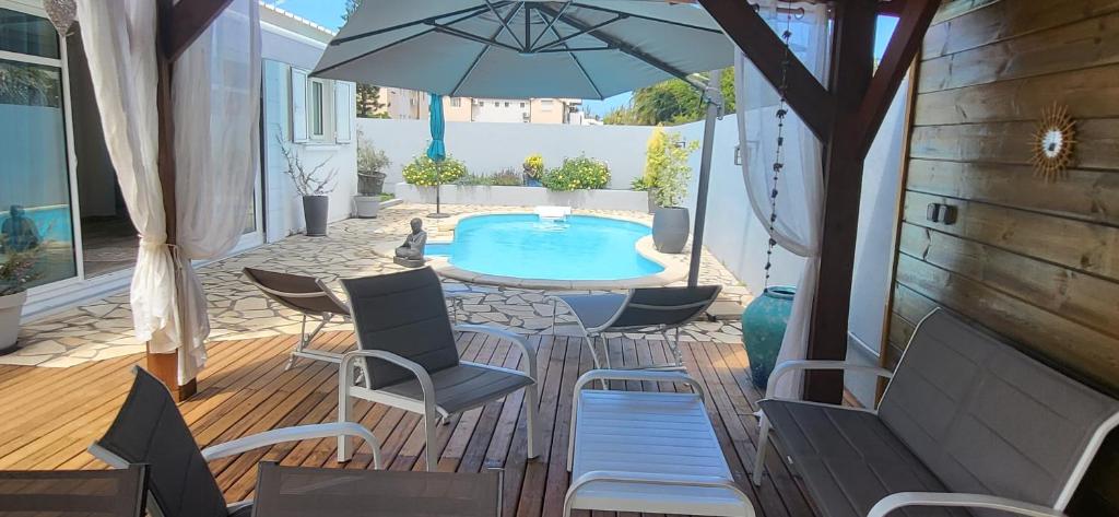 un patio con piscina, sillas y sombrilla en VILLA THALIA à 300 m du lagon de la Saline les Bains, en La Saline-Les-Bains