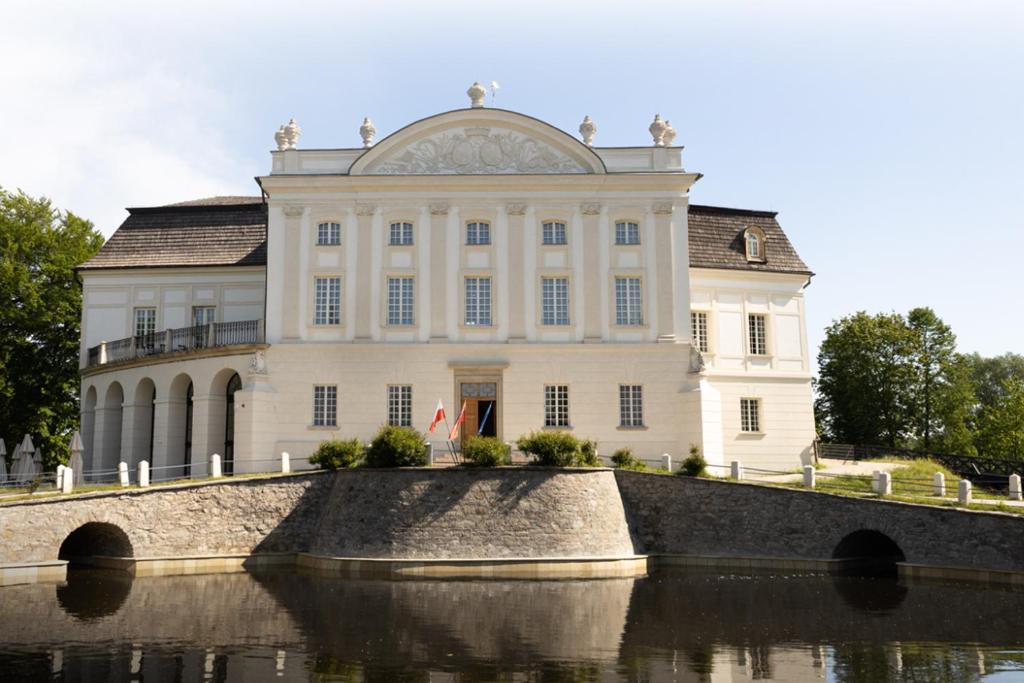a large white building next to a body of water at Pałac w Kurozwękach in Kurozwęki