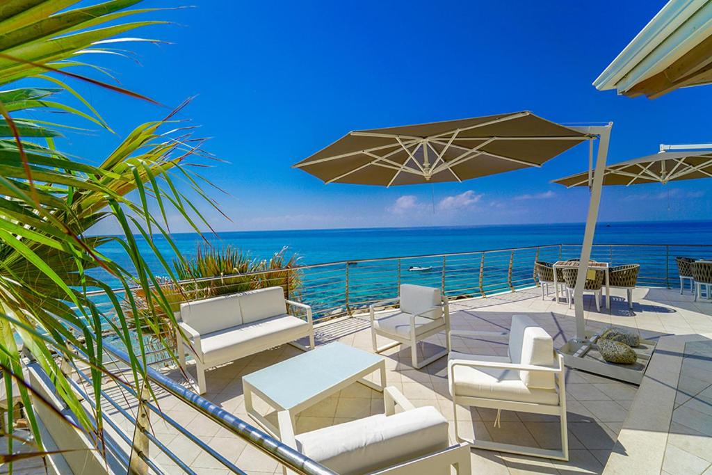 a patio with chairs and an umbrella and the ocean at Baia del Godano Resort & Spa in Capo Vaticano