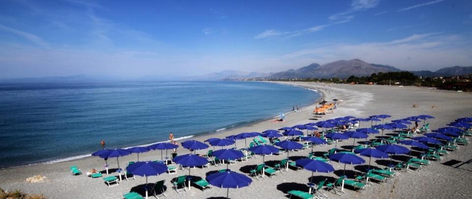 einen Strand mit vielen blauen Sonnenschirmen und dem Meer in der Unterkunft Hotel Guardacosta in Diamante