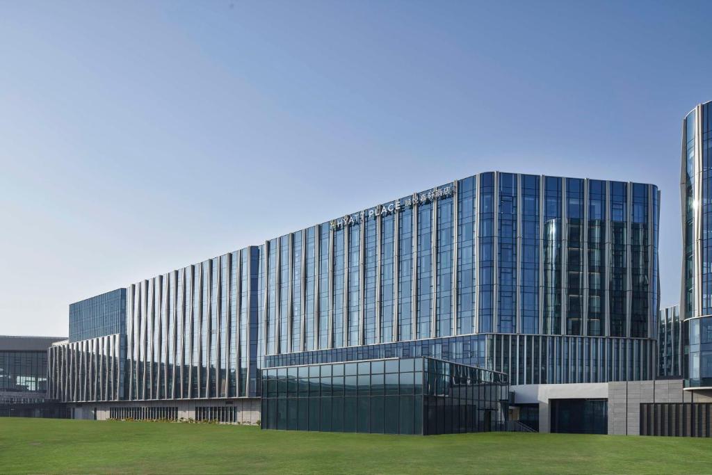 un edificio di vetro alto con un campo verde davanti di Hyatt Place Hangzhou International Airport a Hangzhou