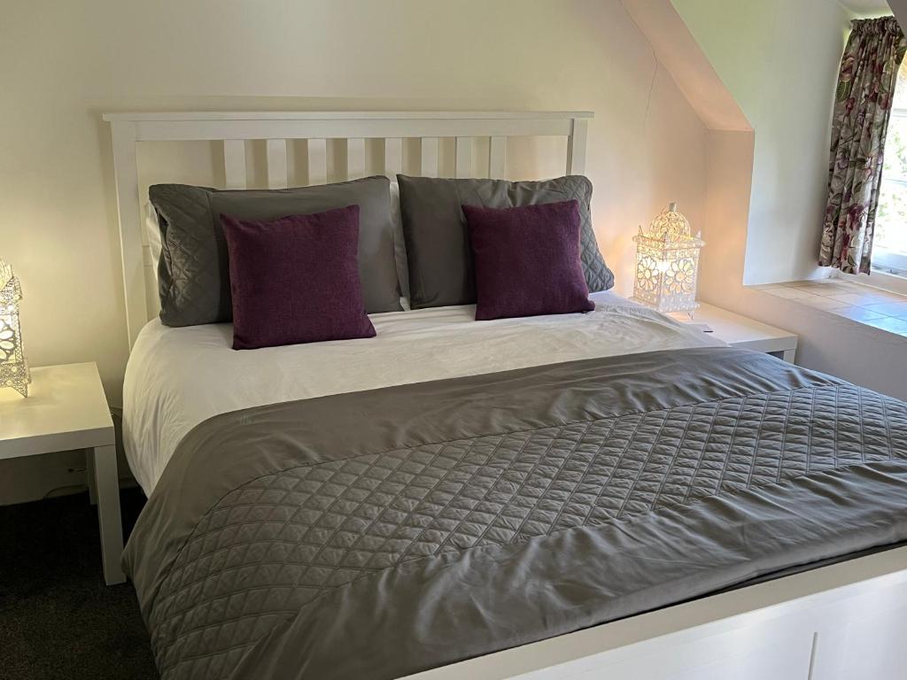 a bedroom with a large bed with purple pillows at Primrose Cottage in Moreton