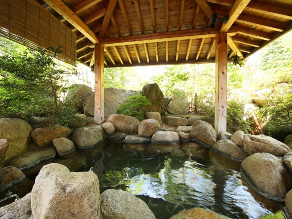 a pond with rocks and a wooden roof at Hotel Yume-no-yu in Omachi