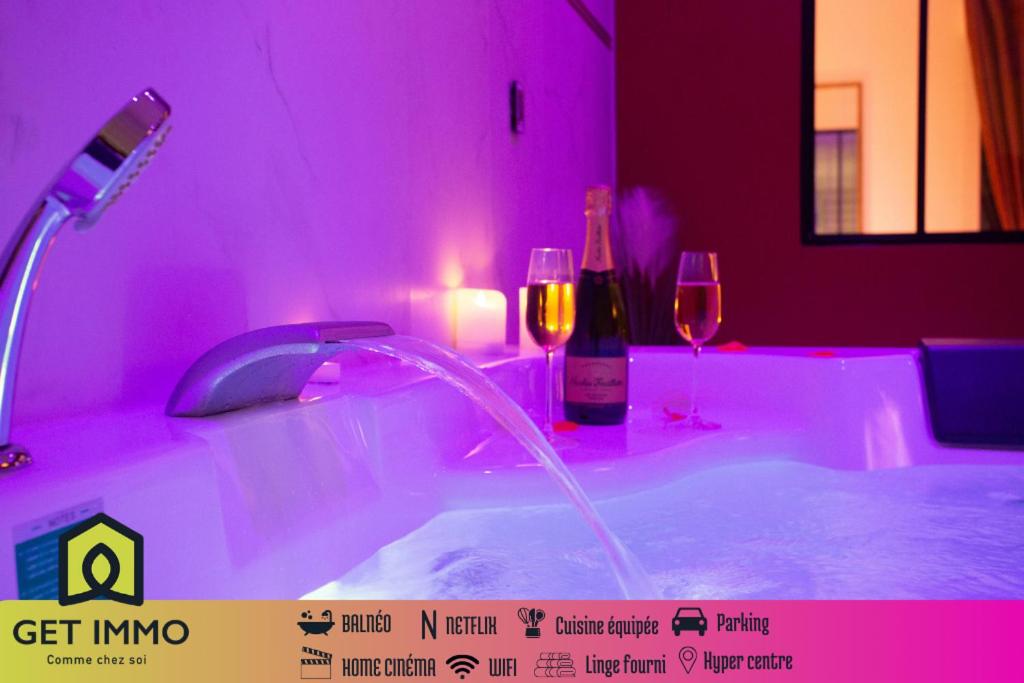 La salle de bains est pourvue d'une baignoire avec éclairage rose et de verres à vin. dans l'établissement Spa & Détente - Cinéma - Parking - Gare, à Amiens