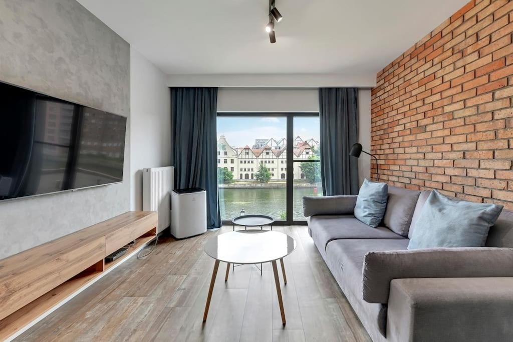 een woonkamer met een bank en een bakstenen muur bij Apartament z widokiem na rzekę by Grand Apartments in Gdańsk