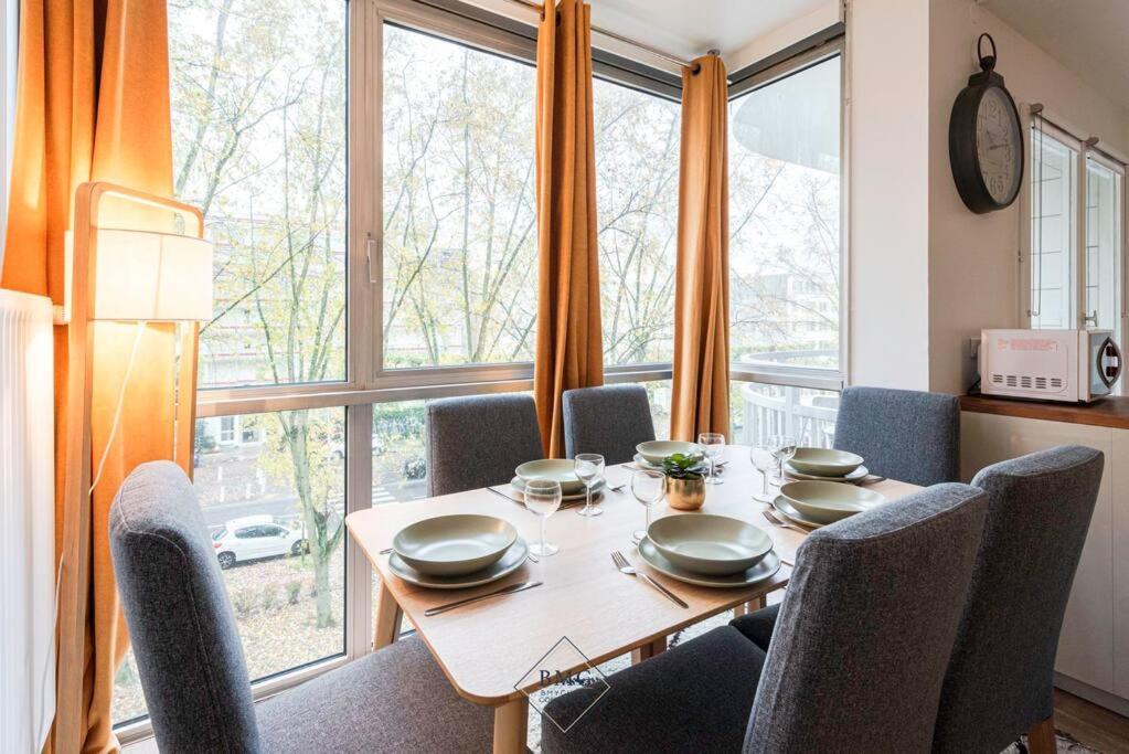 une table de salle à manger avec des chaises et une grande fenêtre dans l'établissement Appartement proche de Disneyland Bmyguest, à Torcy