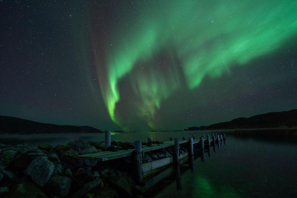 una persona in piedi su un molo sotto l'aurora boreale di Aurora Chase Base 1 a Tromsø