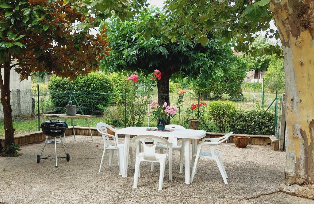 une table et des chaises blanches sous un arbre avec des fleurs dans l'établissement Maison au bord du lac, à Cagnac-les-Mines