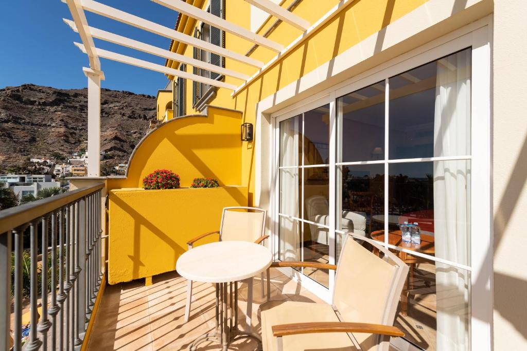 a balcony with a table and chairs and a yellow wall at Hotel Cordial Mogán Playa in Puerto de Mogán