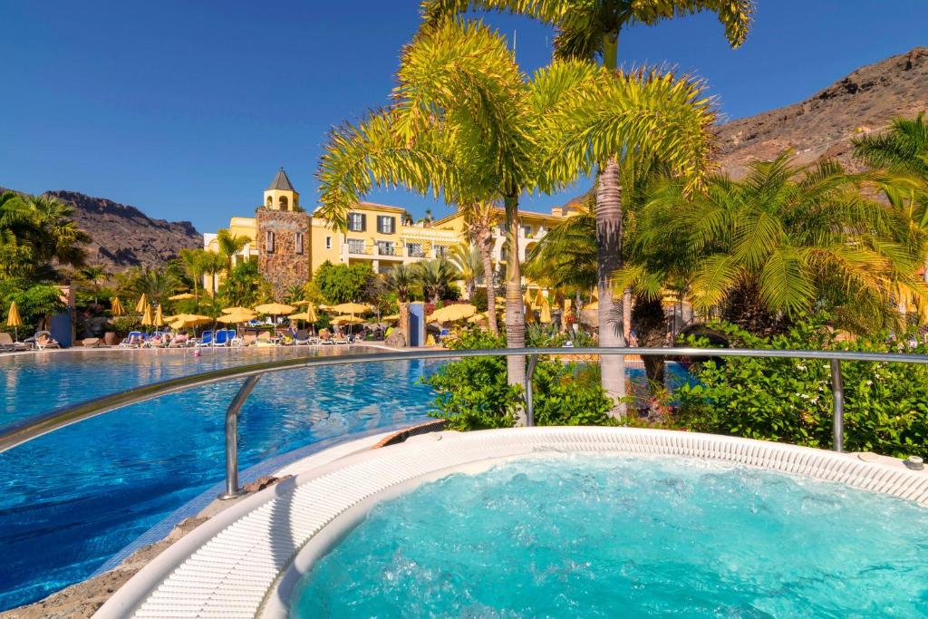 a swimming pool with palm trees and a resort at Hotel Cordial Mogán Playa in Puerto de Mogán