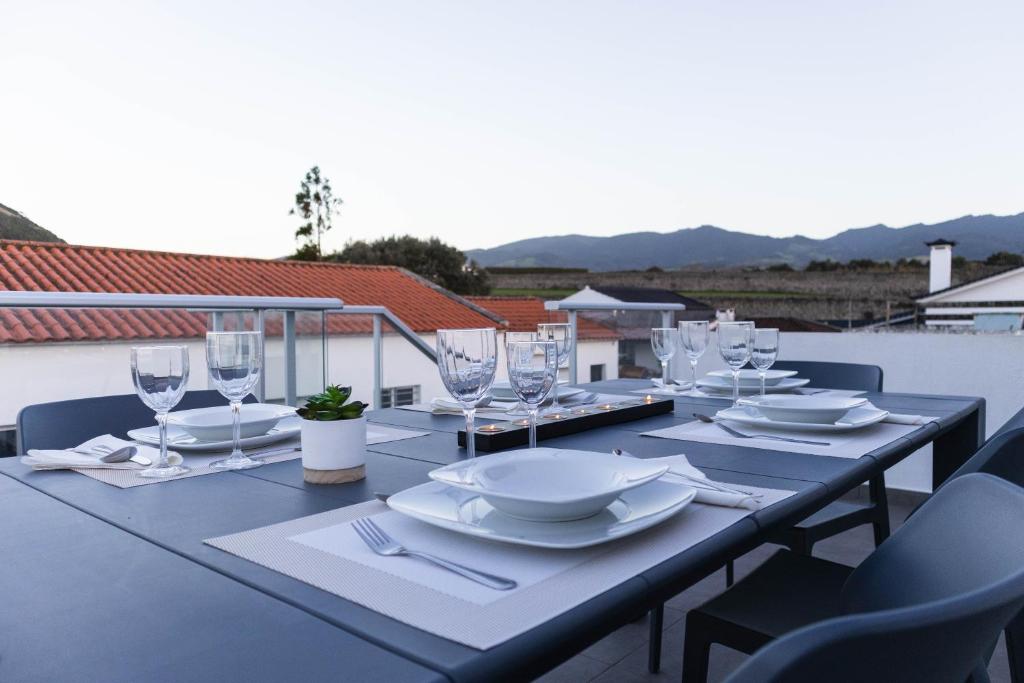 a table with plates and wine glasses on a balcony at By the hill in Ribeira Grande