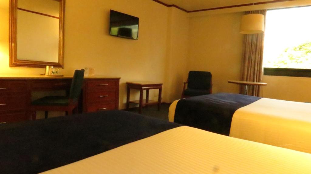 A warmly decorated twin room with a dresser desk and broad window.
