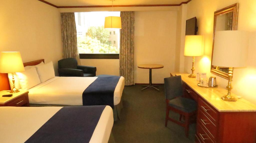 A two-bed room with a broad window, armchair, and long wooden desk.