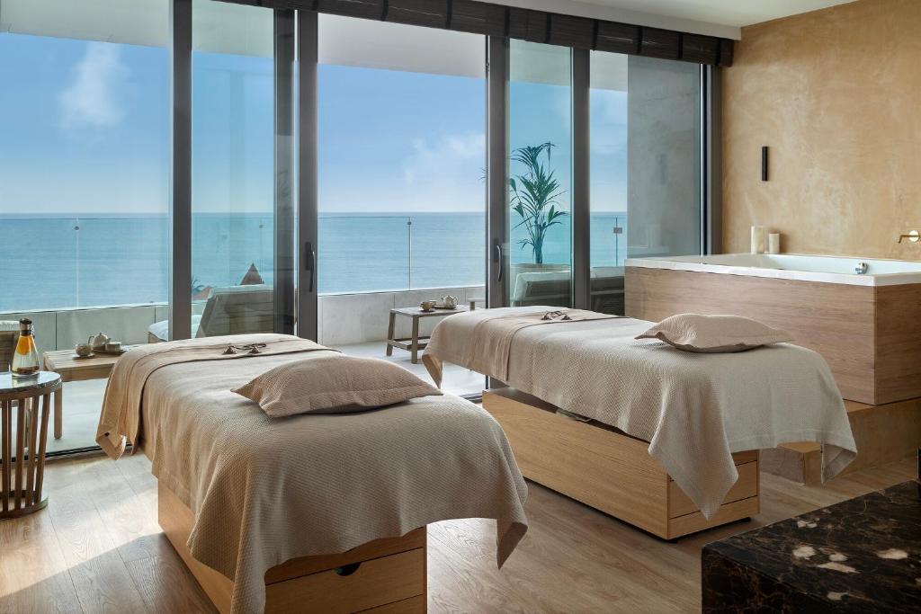 two beds in a room with a bath tub and the ocean at EVOLUTION Cascais-Estoril Hotel in Estoril