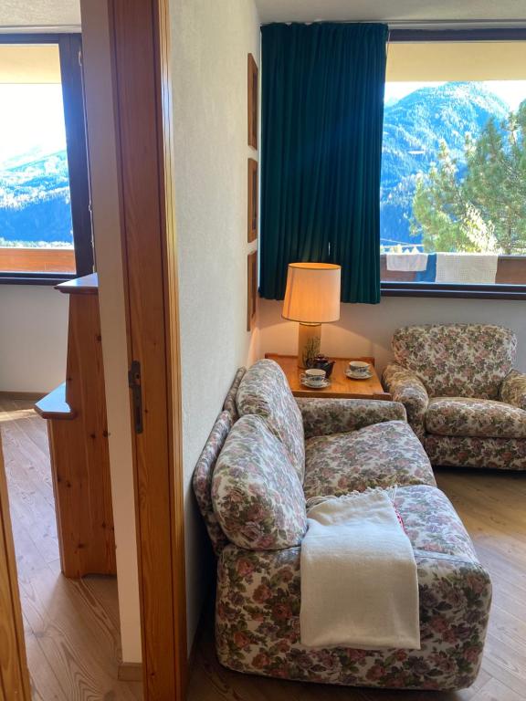 a living room with a couch and a chair and windows at Encia's Home Dolomiti in Castello di Fiemme
