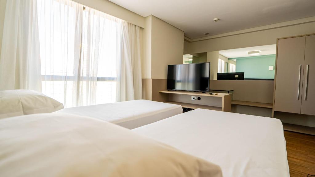 a hotel room with two beds and a flat screen tv at Roomo Praia de Boa Viagem Residencial in Recife