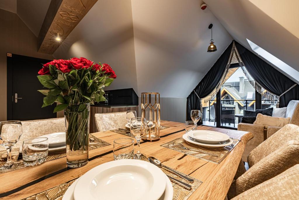 Dining table set with plates and vase of red roses, balcony view beyond.