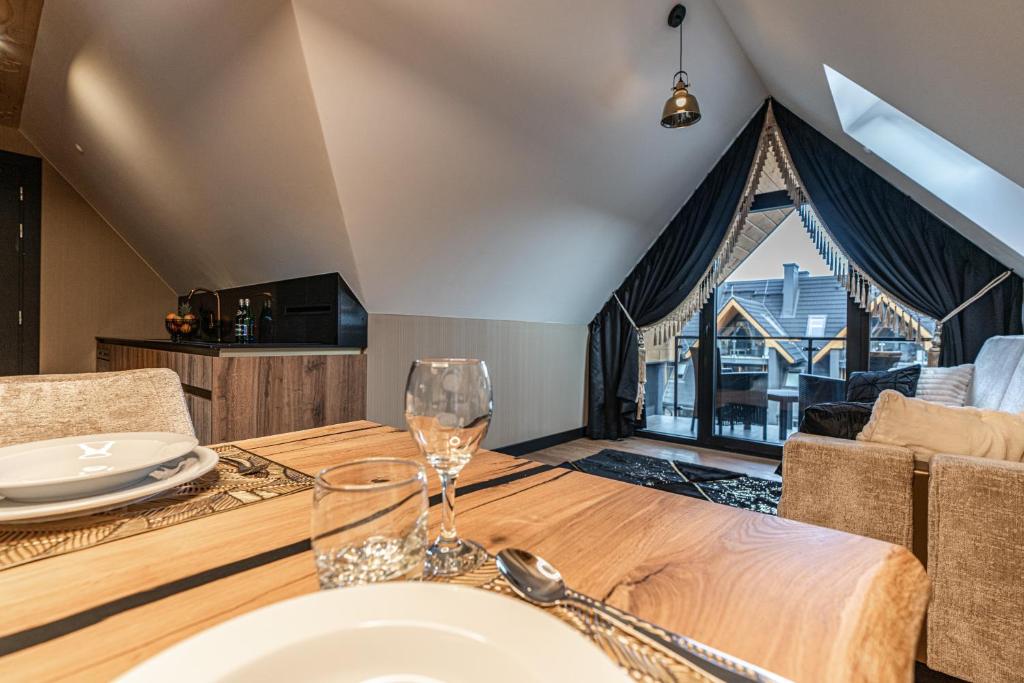 Dining table foreground with glassware, view toward balcony and seating area under sloped ceiling.
