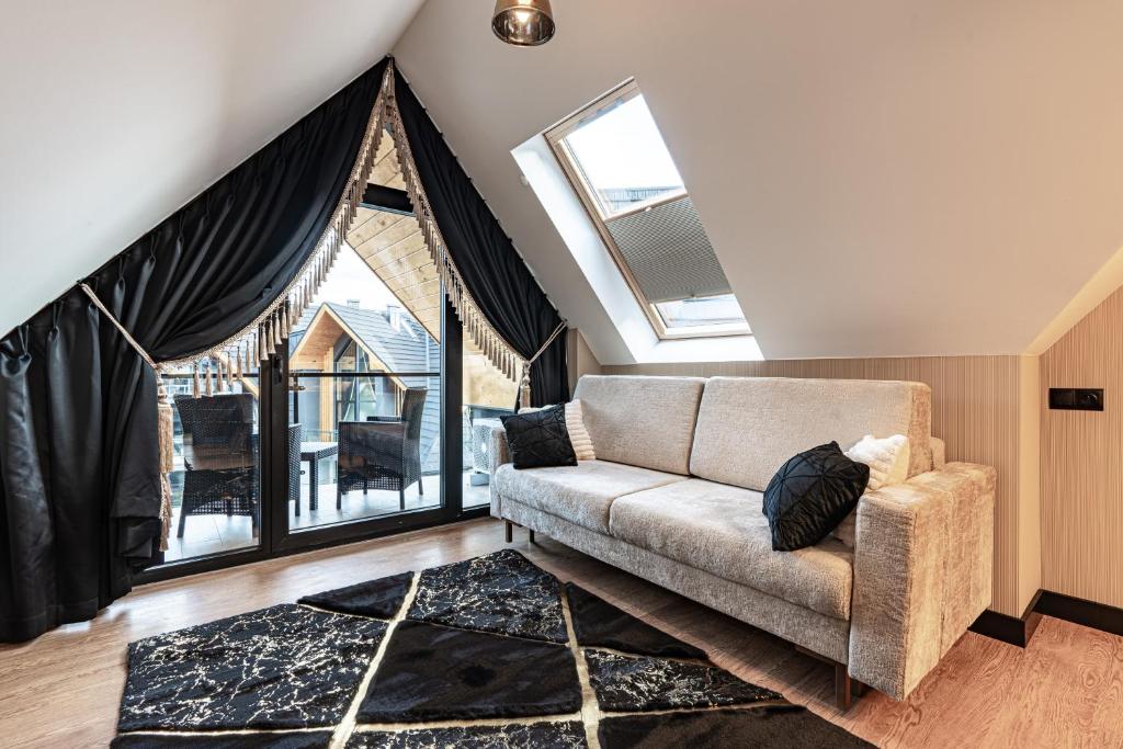 Cozy attic sitting area with beige sofa, skylight, black geometric rug and balcony doors.