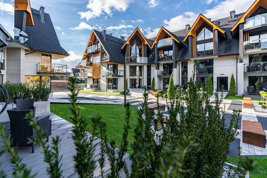 Courtyard view of modern chalet-style buildings with balconies, landscaped greenery, sunny sky.