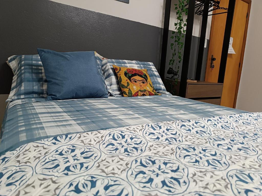 a bed with a blue and white comforter and a pillow at Apezinho 209 in São Leopoldo