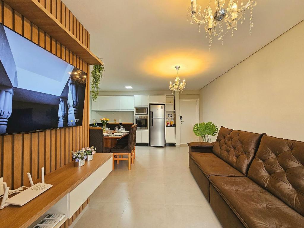 a living room with a brown couch and a kitchen at Apt Novíssimo 3quartos 2vagas garagem prox centro in Foz do Iguaçu