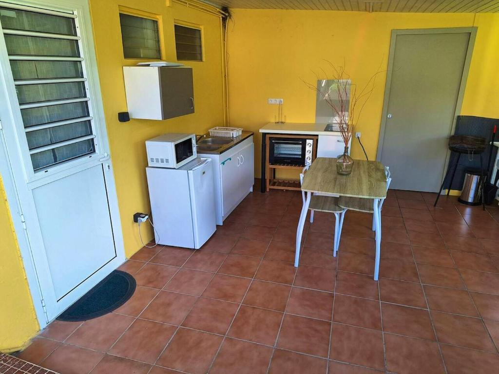 una cucina con pareti gialle, tavolo ed elettrodomestici di Studio avec terrasse et wifi a Le Marin a 5 km de la plage a Le Marin