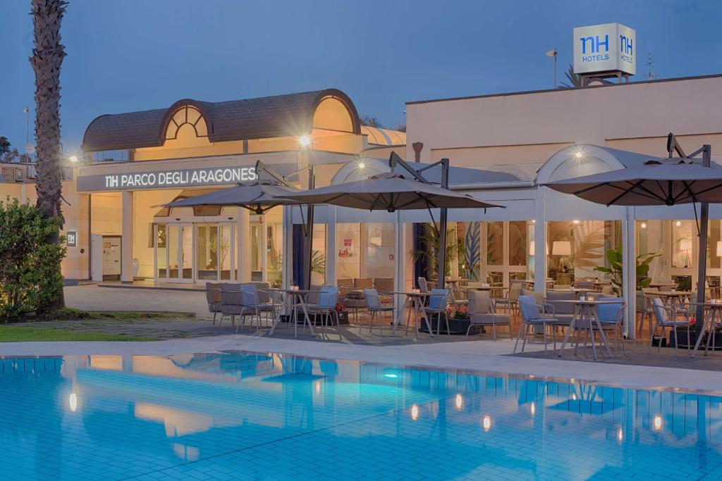 un hotel con piscina, mesas y sombrillas en NH Catania Parco degli Aragonesi, en Catania