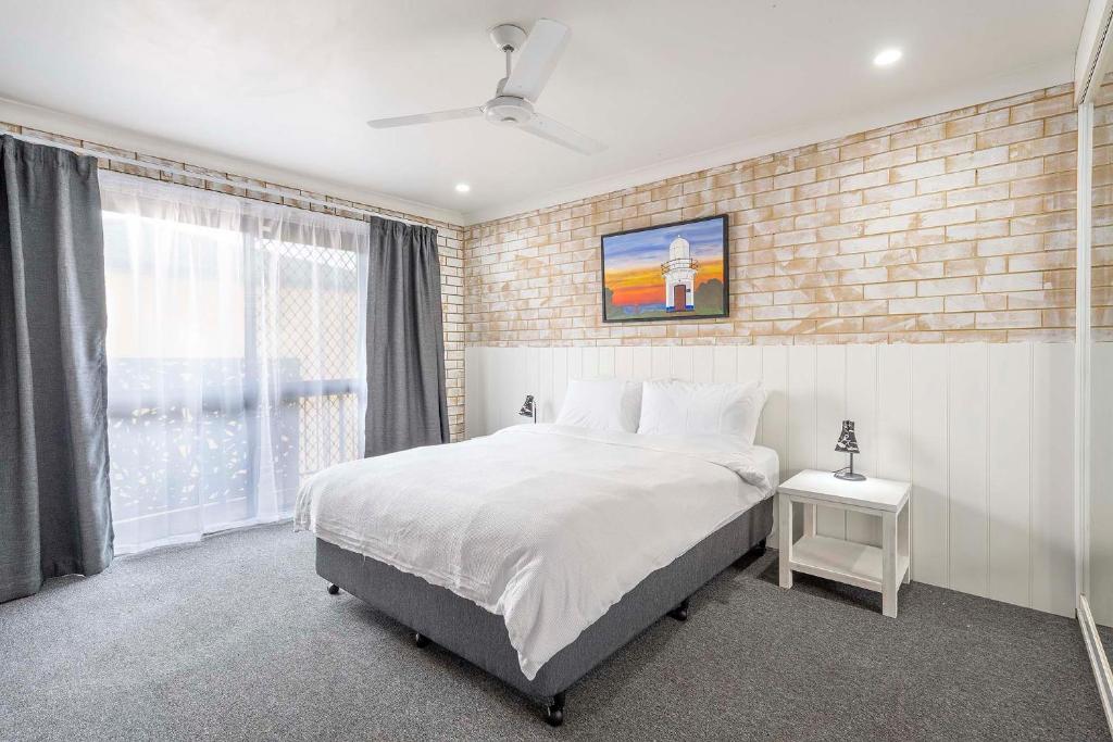 - une chambre avec un lit blanc et un mur en briques dans l'établissement Coast Inn Motel, à Ballina