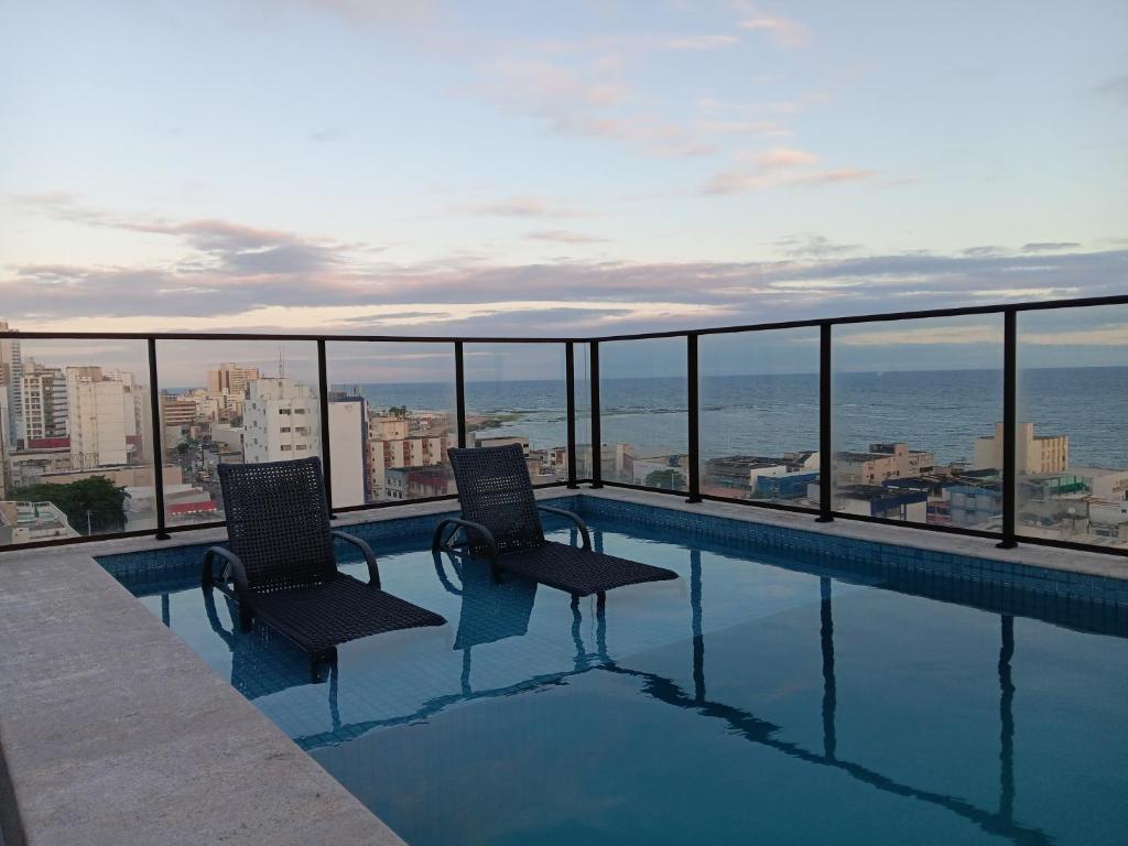 a swimming pool with two chairs and a view of the ocean at Apartamento novo, perto da praia e conveniências in Salvador