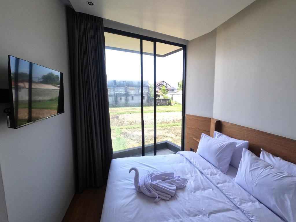 a bedroom with a white bed with a large window at The Fields Hotel and Apartment in Seminyak