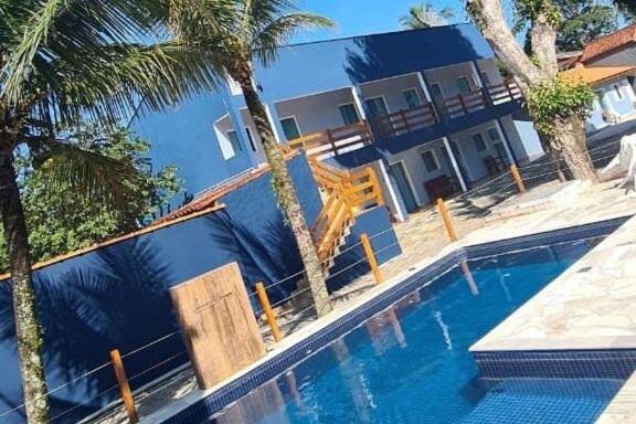 a swimming pool next to a blue building with palm trees at Maresias Flat's Unidade II in Maresias