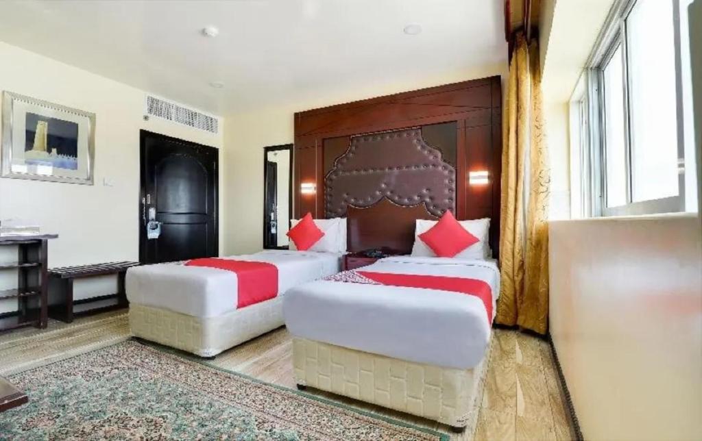 SHH Hotel في الفجيرة: سريرين في غرفة الفندق مع وسائد حمراء
