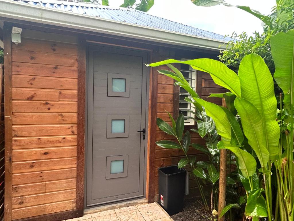 un garaje de madera con una puerta en un jardín en Joli bungalow fleuri, en Les Abymes