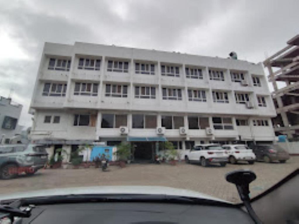 duży biały budynek z samochodami zaparkowanymi przed nim w obiekcie Hotel Embassy International,Latur w mieście Lātūr